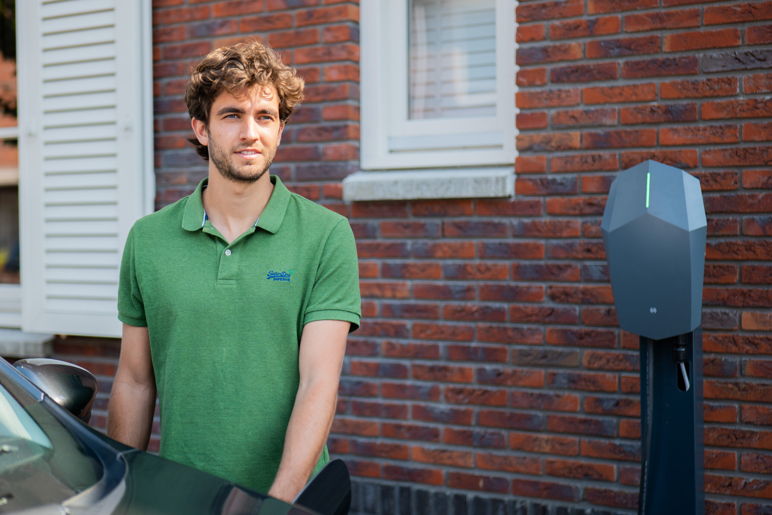 Person in a green polo standing by a house looking at a Volt Time Source 2S charger.